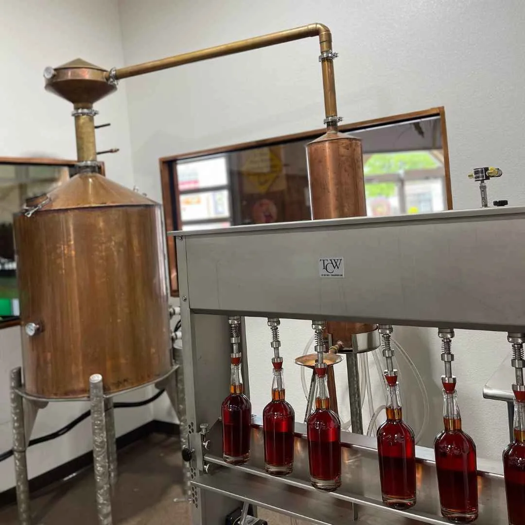 Heart River Rum being bottled by hand beside the copper still