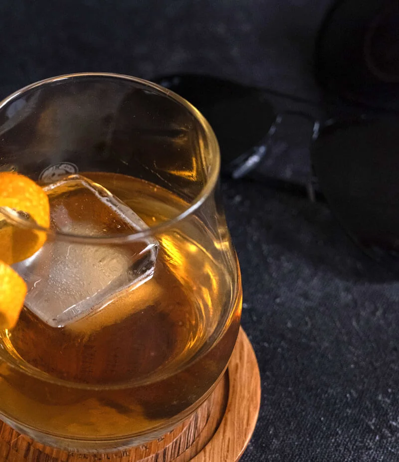 Old fashioned cocktail with an orange peel twist on a wooden coaster