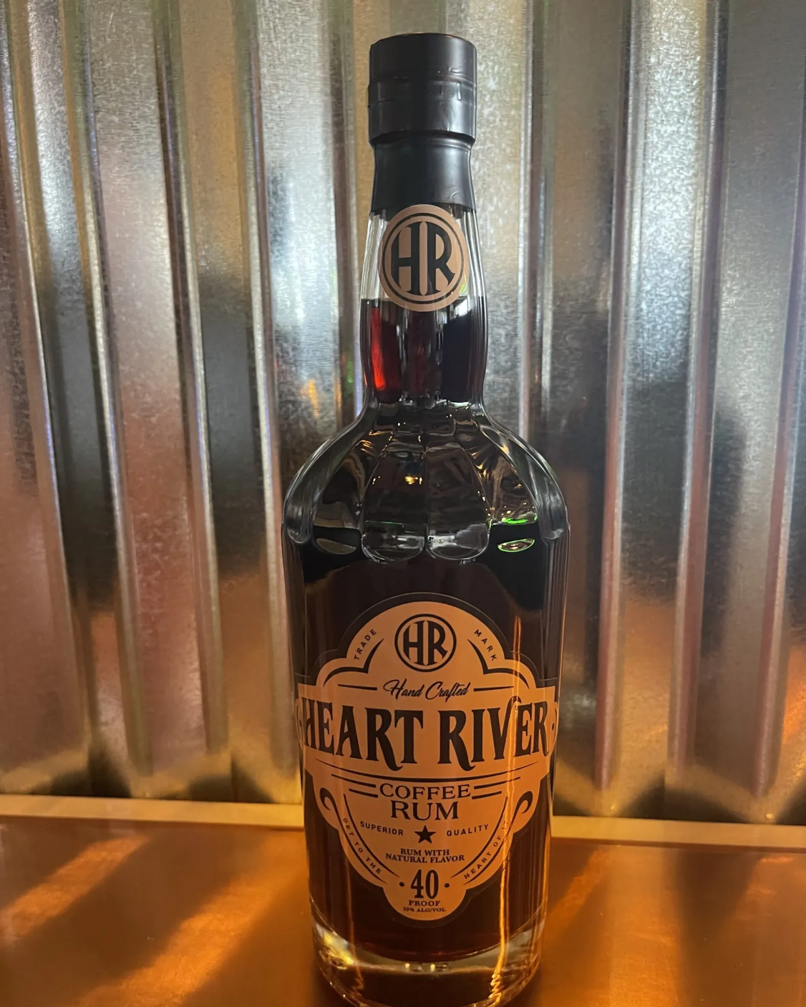 Bottle of Heart River Rum glowing in warm amber light against corrugated metal